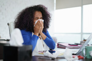 Woman in the office blowing her nose due to allergies.